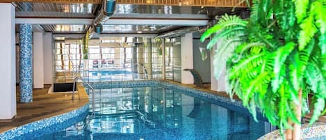 An indoor swimming pool with clear glass walls, a wooden ceiling, and a potted plant.