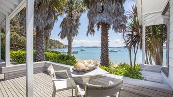 A covered outdoor seating area with a table set for two, overlooking a body of water with boats.