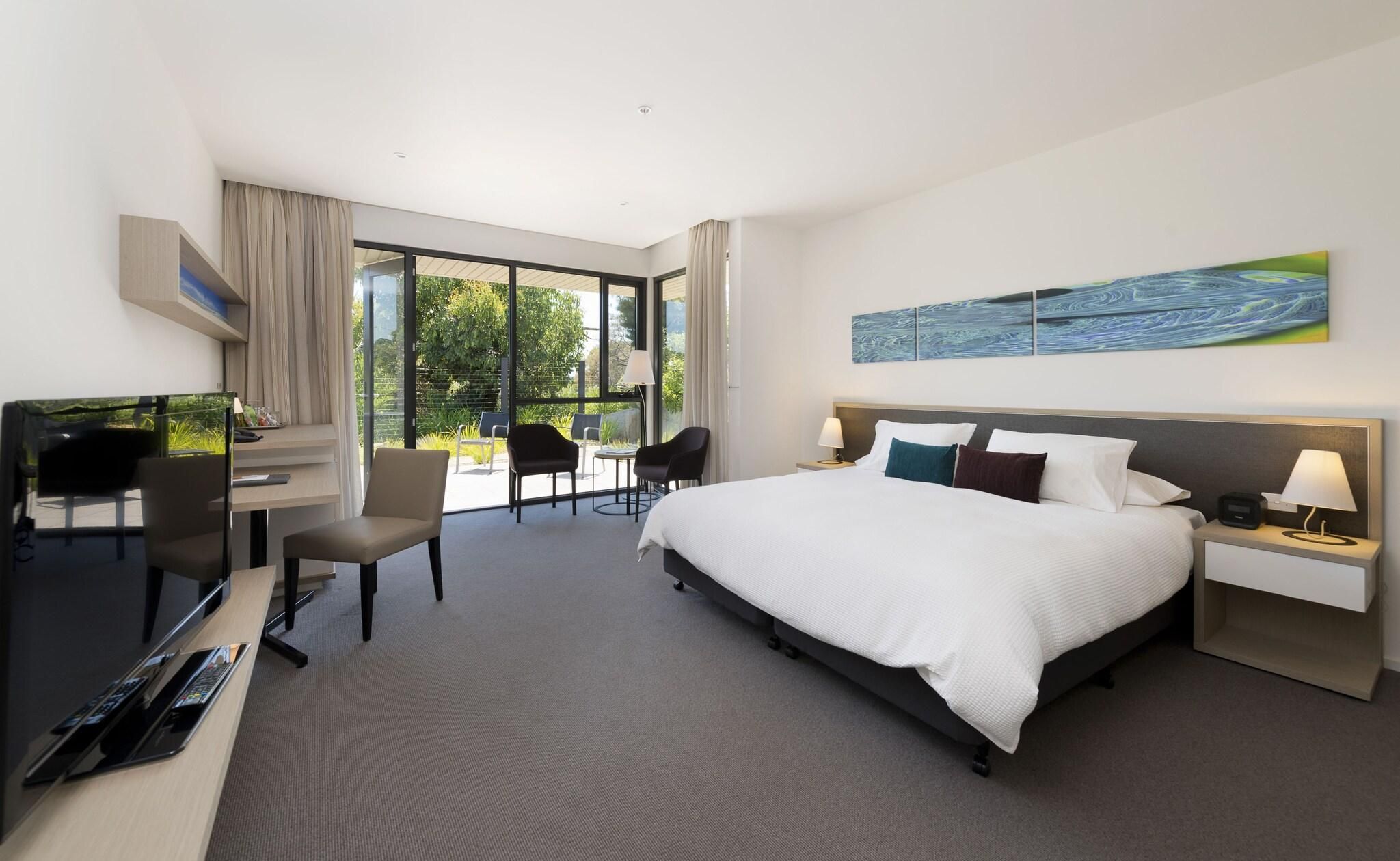 A hotel room with a bed, desk, chairs, and a large window.
