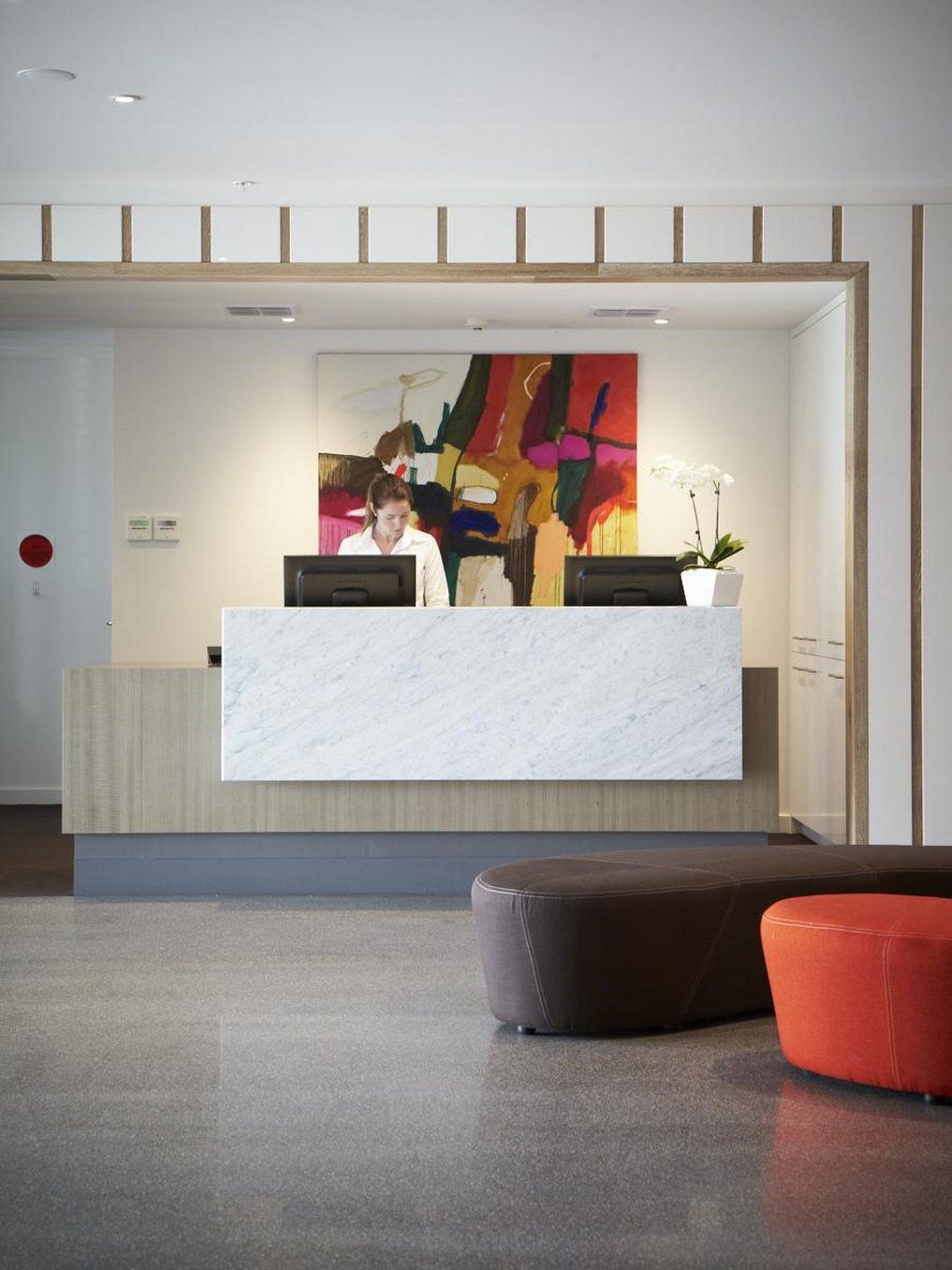 A reception desk with a marble top, a colorful abstract painting, and a potted plant.