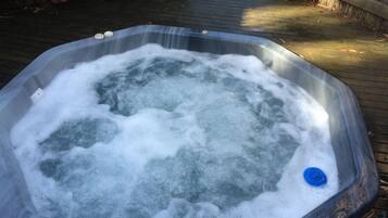 A hot tub filled with water and bubbles, surrounded by a wooden deck.