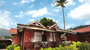 A two-story building with a red facade and a balcony, surrounded by greenery and a palm tree. - Paya Beach Resort (Tioman Island)