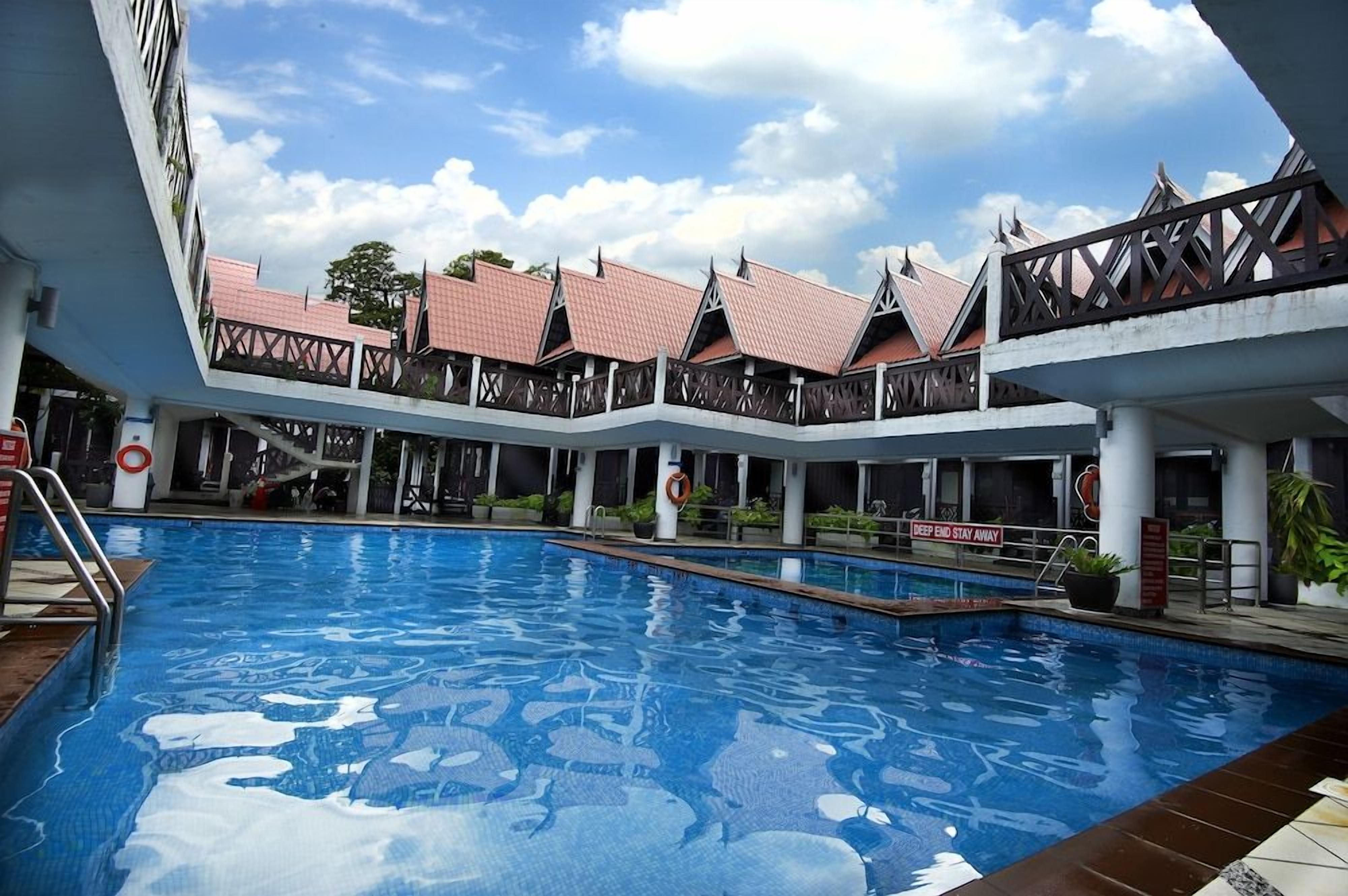 A swimming pool with a clear blue water surface, surrounded by a covered area with multiple levels and a roofed structure.