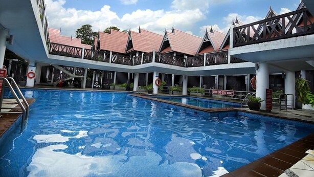 A swimming pool with a clear blue water surface, surrounded by a covered area with multiple roofed structures. - Paya Beach Resort (Tioman Island)