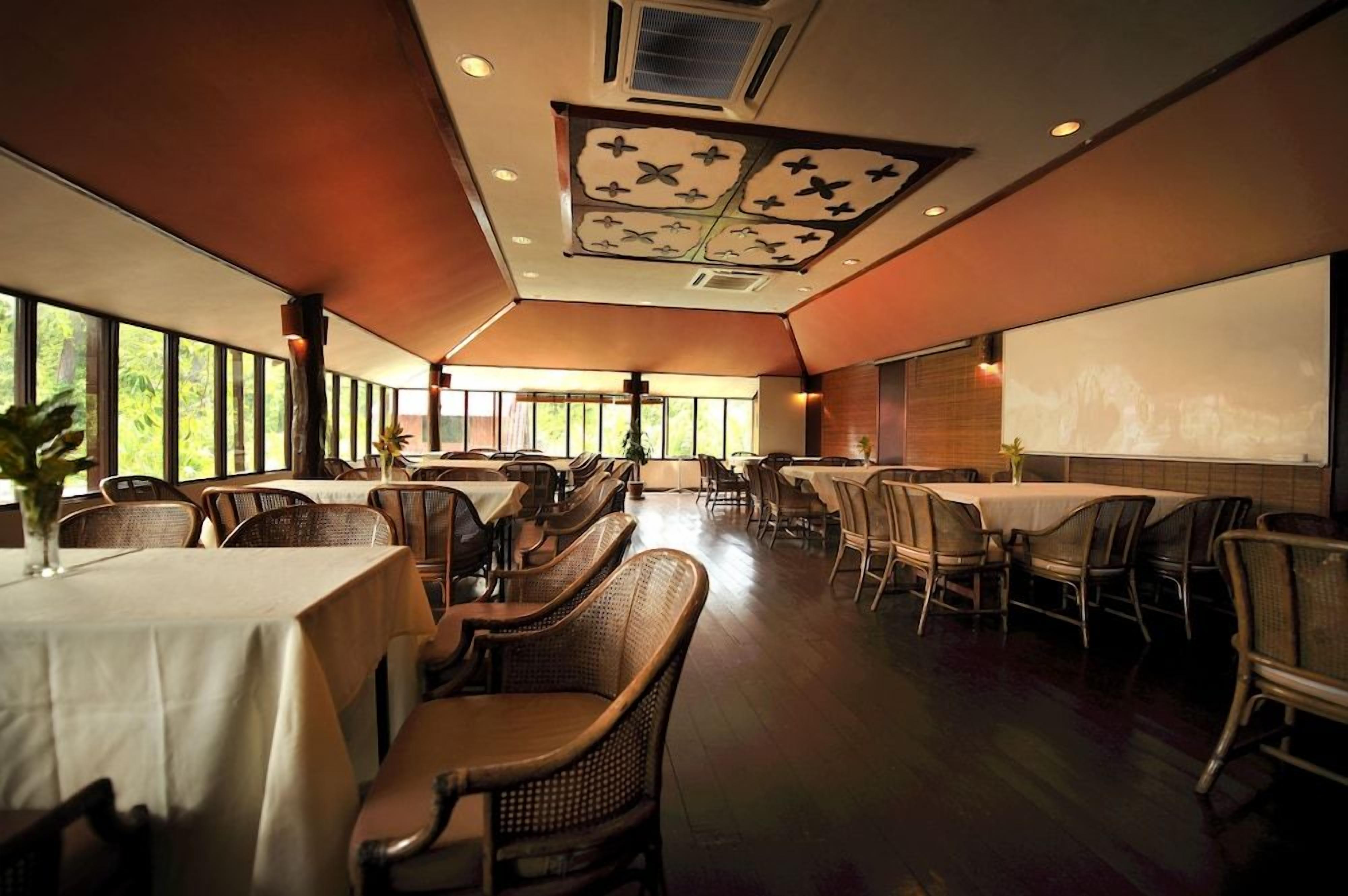 A spacious dining area with high ceilings, large windows, and a projector screen on the wall.
