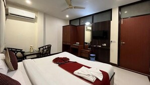 A hotel room with a bed, a desk, a chair, a wardrobe, and a ceiling fan. - Hotel S R Palace (Agra)