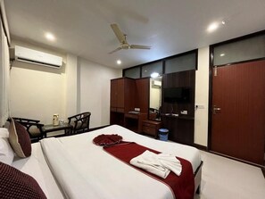 A hotel room with a bed, a desk, a chair, a wardrobe, and a ceiling fan. - Hotel S R Palace (Agra)