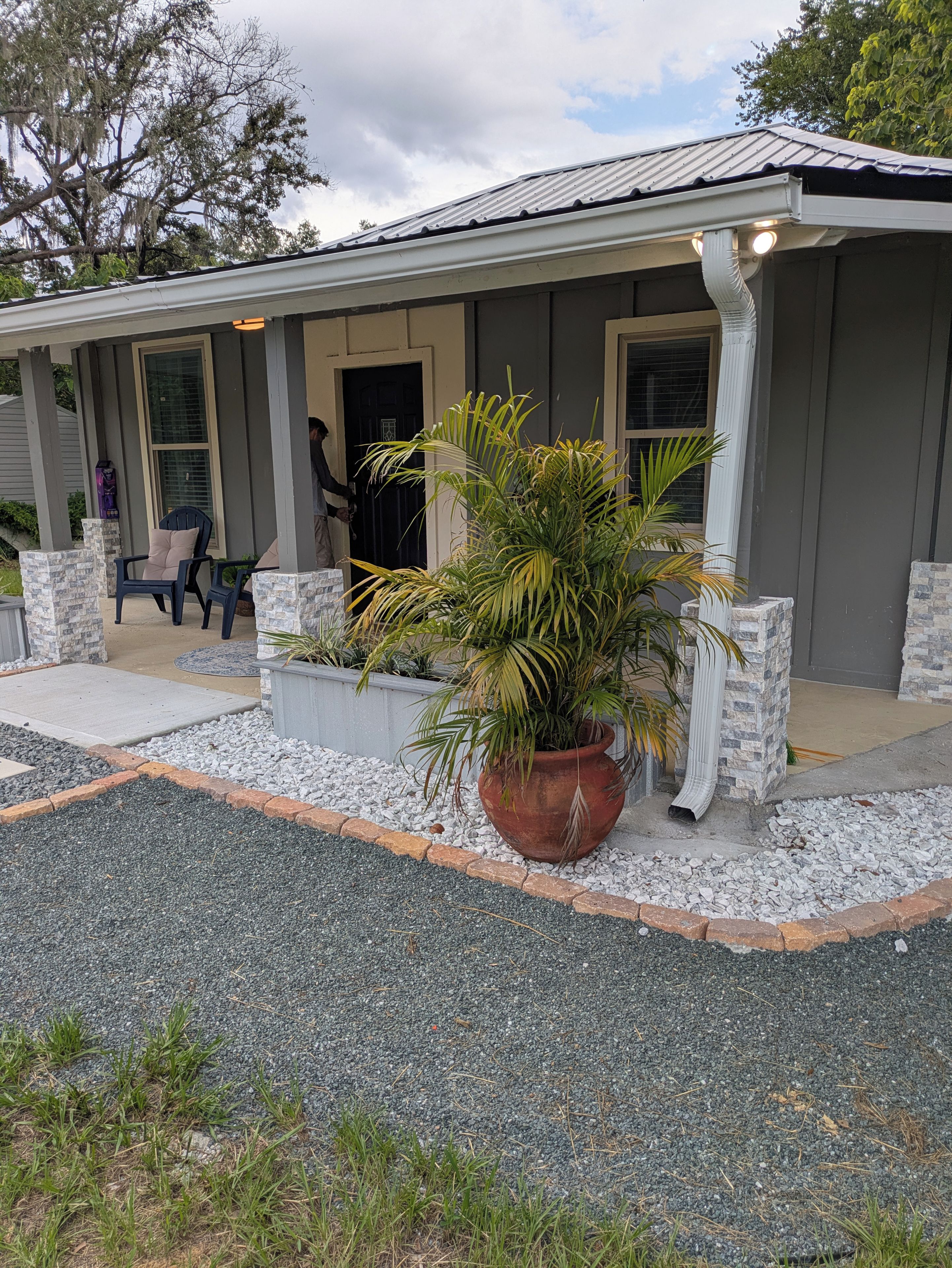 A house with a porch, a large potted plant, and a chair.