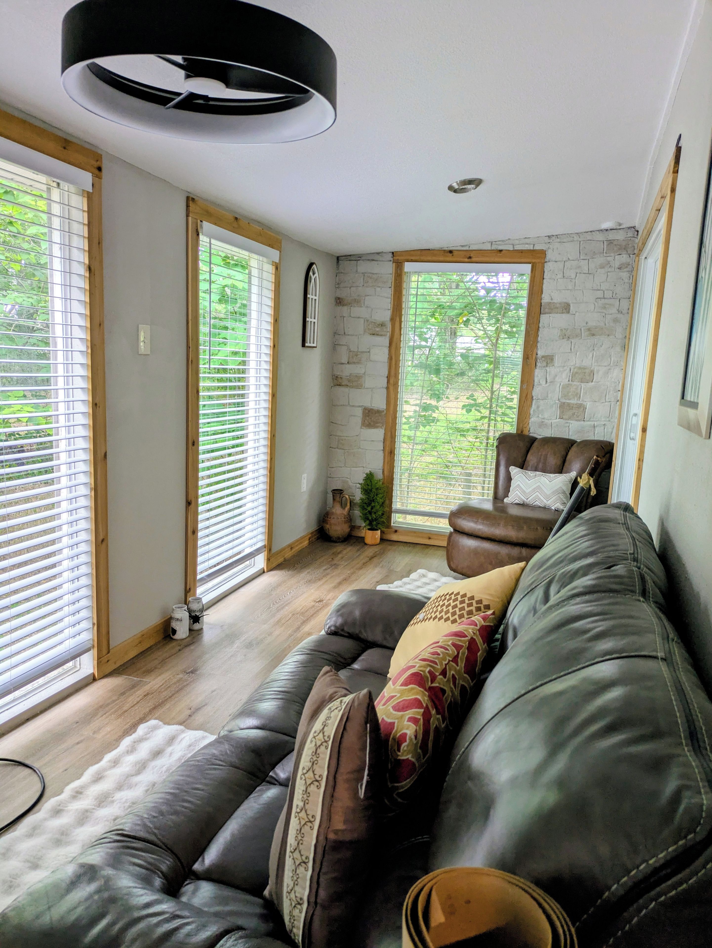 A modern living room with a leather sofa, a wooden-framed window, and a stone wall.