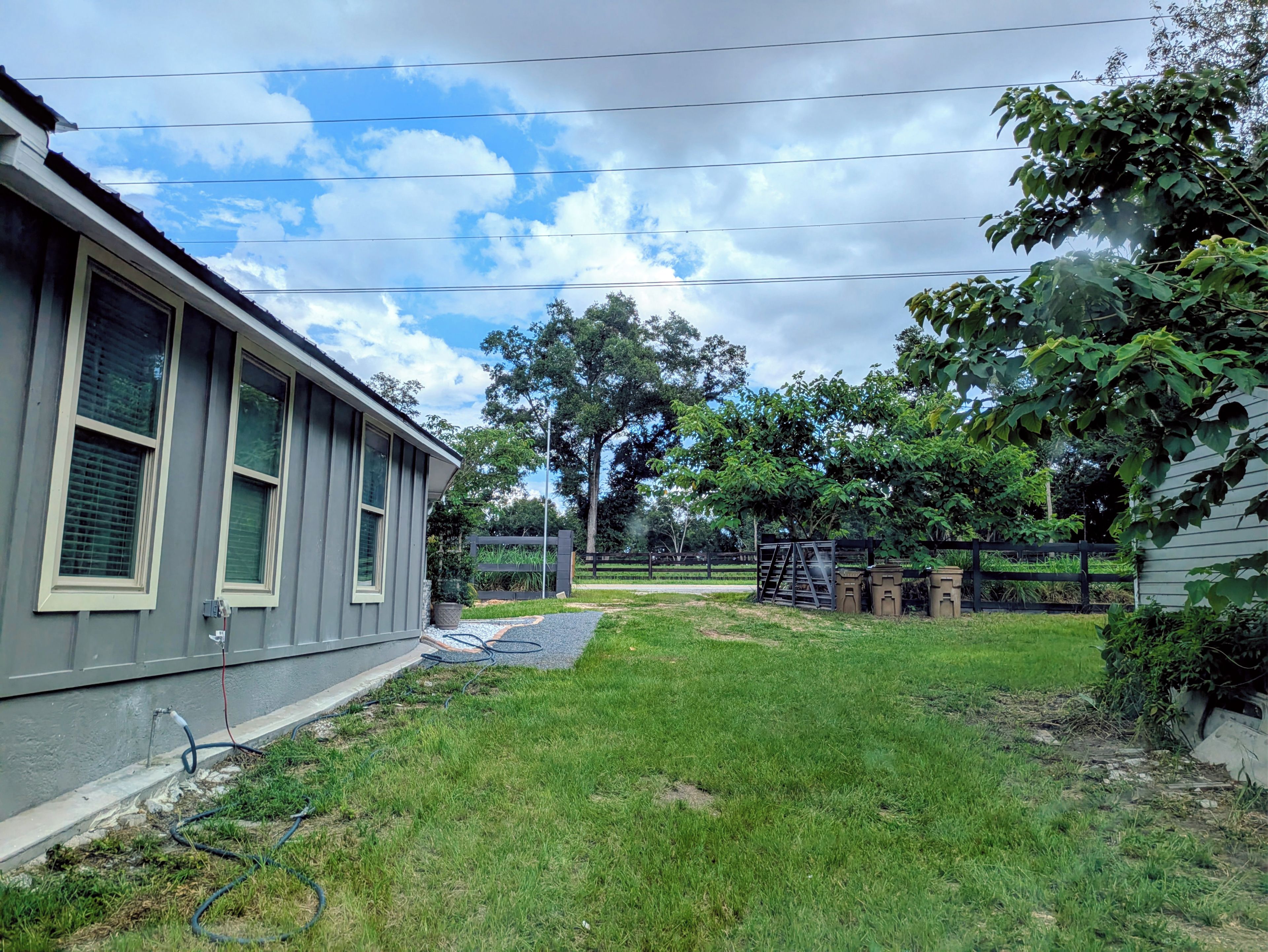 A residential property with a grassy yard, a wooden fence, and a house with a grey exterior.