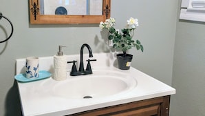 A bathroom with a white sink, wooden cabinet drawers, a mirror with a wooden frame, a potted plant, and a blue cup on the counter. - 3-bedroom bungalow in Clermont ,25 miles to Disney (Clermont)