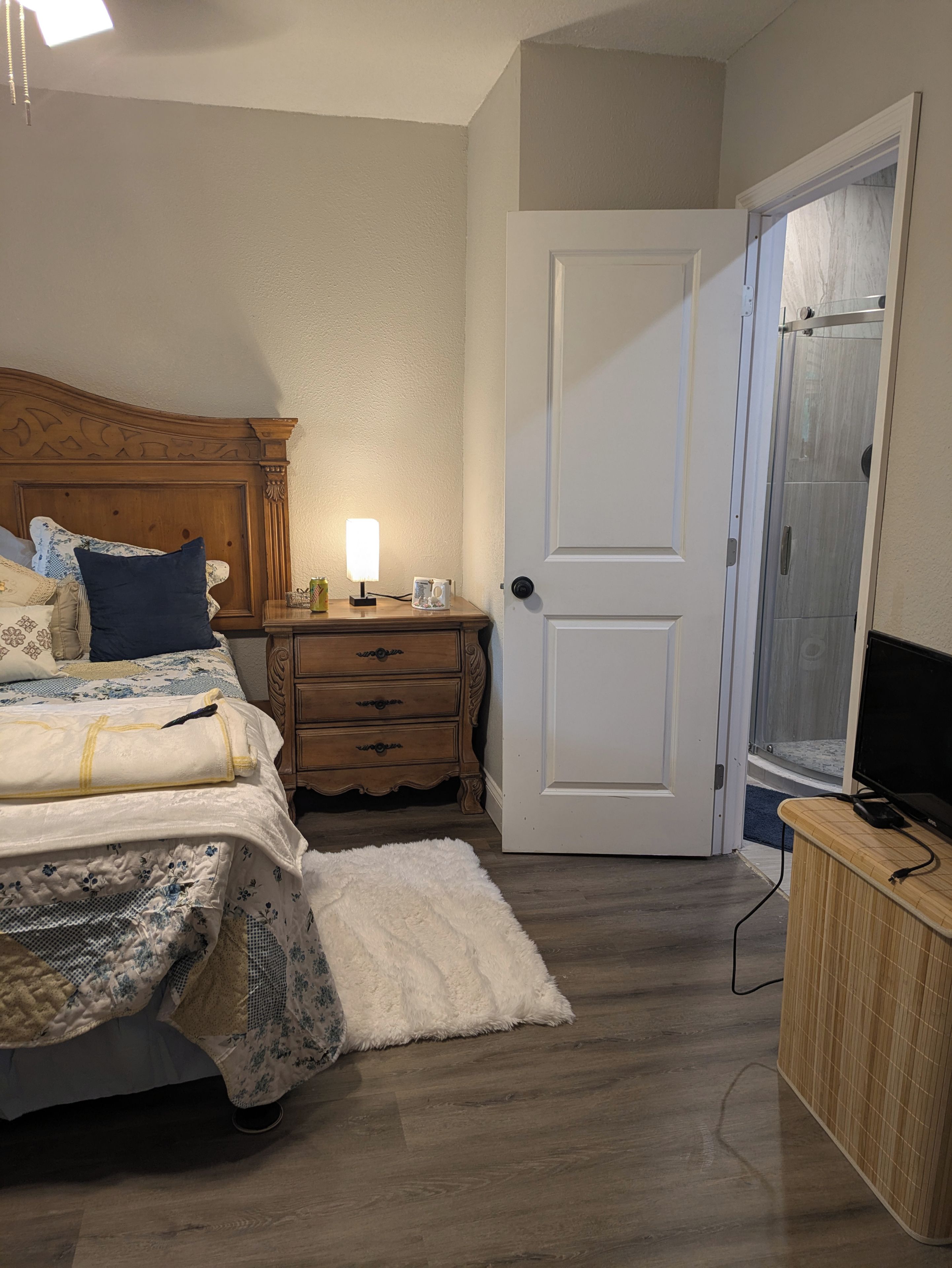 A bedroom with a bed, bedside table, lamp, and a door leading to a bathroom.