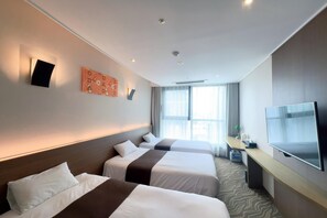 Quarto de hotel com duas camas, televisão de tela plana, escrivaninha com cadeira e uma grande janela com cortinas.