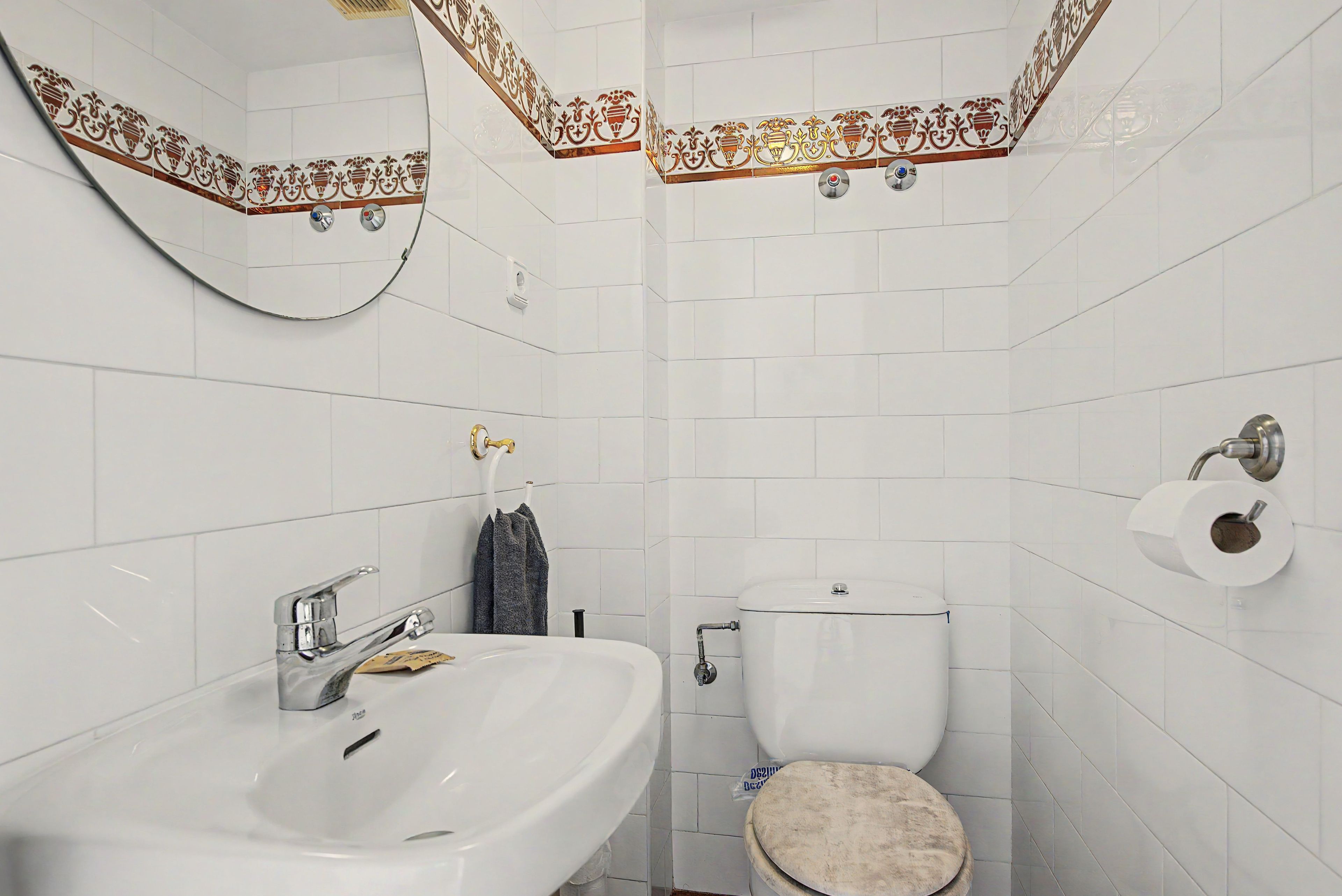 Een badkamer met een witte wasbak, toilet en een spiegel met decoratieve tegels.
