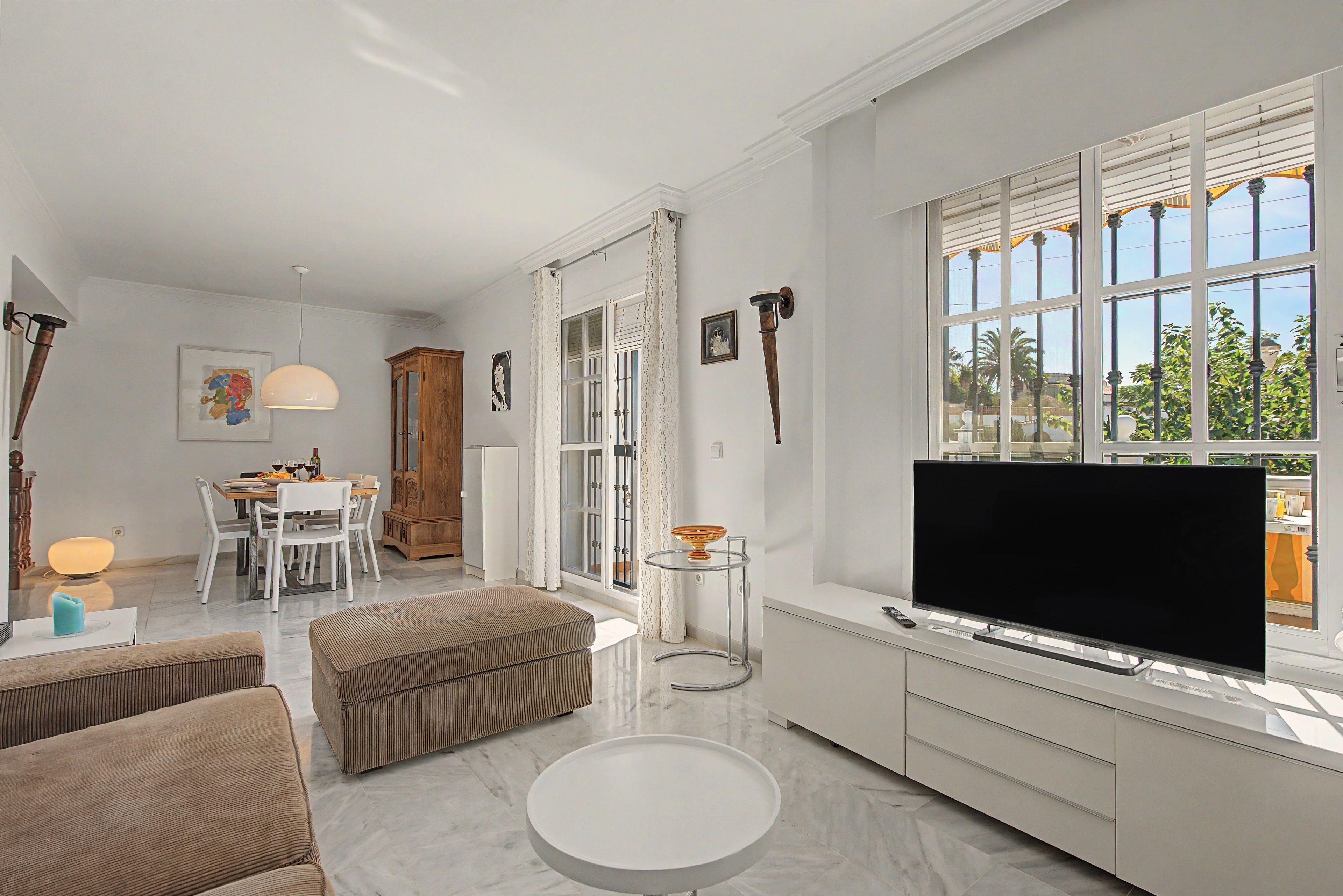 Ein modernes Wohnzimmer mit Flachbildfernseher, einem Essbereich mit Tisch und Stühlen sowie einer Küchenzeile mit Fenster.