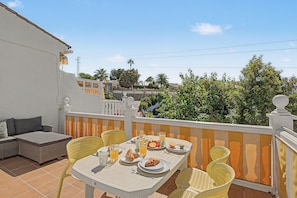 A terrace with a table set for breakfast, outdoor seating, and a view of the neighborhood.