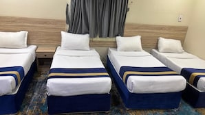 A hotel room with four single beds, each with a blue and white bedspread, arranged in a row. - Sadan Hotel (Al Aziziyah)