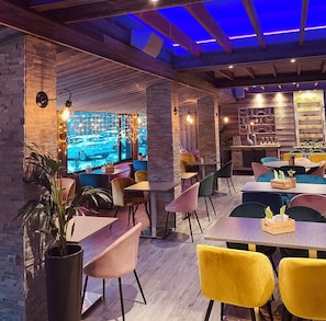 A modern restaurant with exposed brick walls, wooden beams, and a variety of colorful chairs and tables. - Hotel Le Panorama (Mont-Dore)