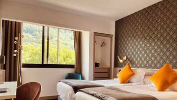 A hotel room with two beds, a desk, a chair, and a large window with a view of trees.
