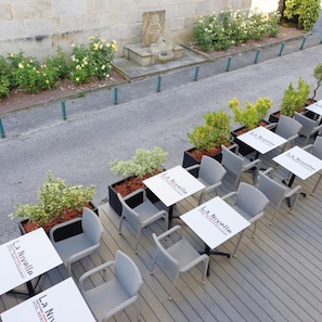 Udendørs siddepladser med borde og stole, nogle med planter.