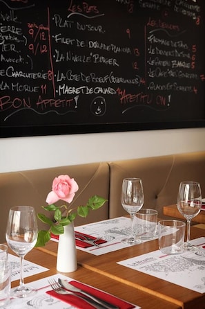 En restaurantscene med en menutavle, en vase med en lyserød blomst og tomme vinglas på et bord.