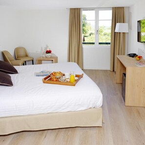 A hotel room with a bed, a desk, a chair, a TV, and a window with curtains. - Hotel De La Nivelle (Saint-Pee-sur-Nivelle)