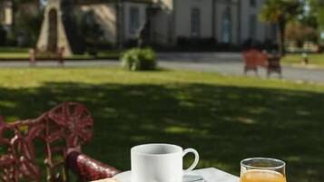 A table with croissants, bread, strawberries, a glass of juice, and a cup, set outdoors with a building in the background.