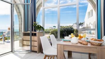 Un comedor con vistas al mar, una mesa dispuesta para el desayuno y un balcón con una silla.
