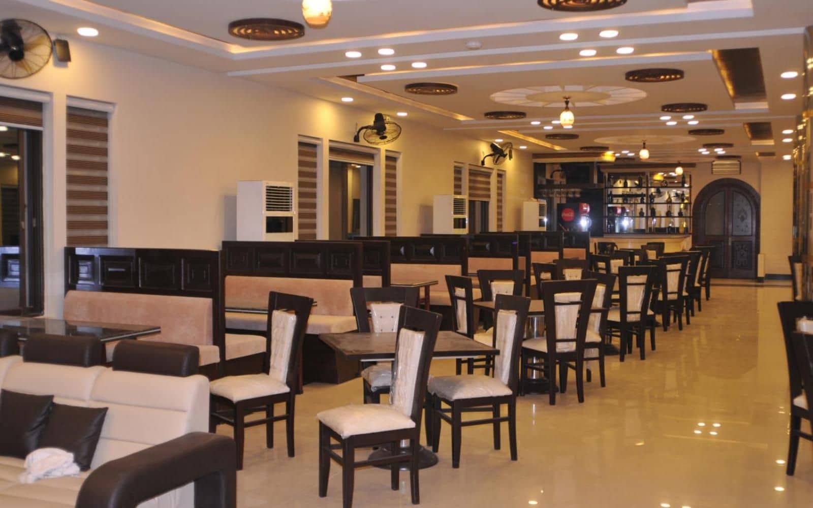 Un hall d’hôtel doté de plusieurs espaces de détente, comprenant des canapés et des tables, et un bar situé au fond de la pièce.