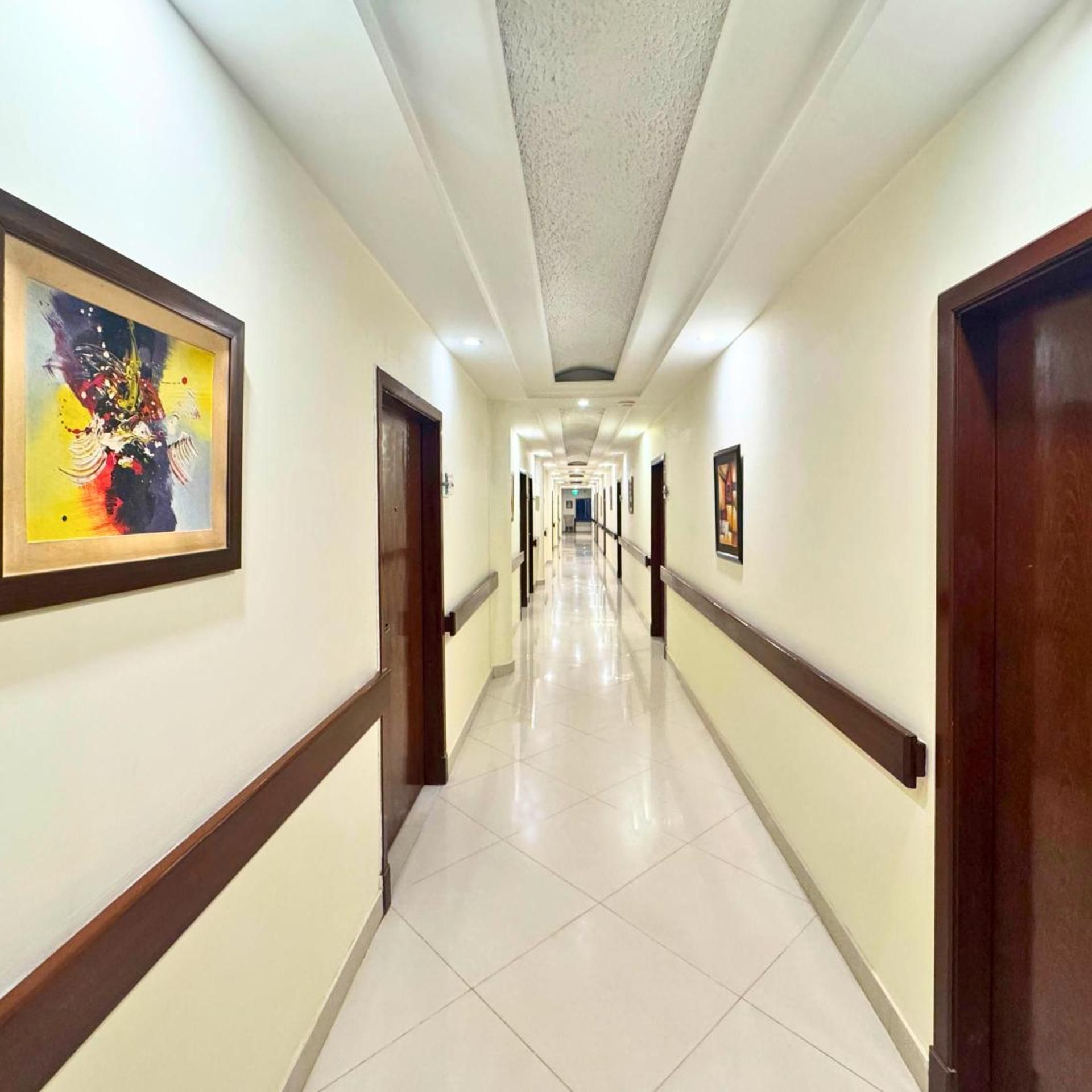 A hotel corridor with a tiled floor, wooden doors, and framed artwork on the walls.