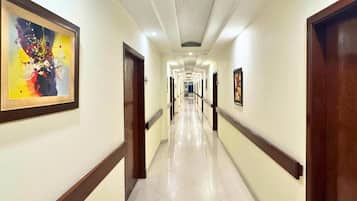A hotel corridor with a tiled floor, wooden doors, and framed artwork on the walls.
