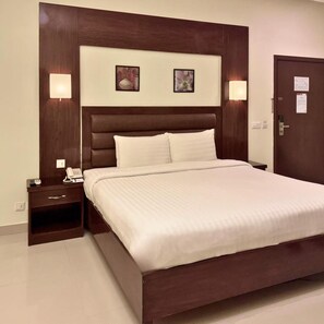 A hotel room with a large bed, a nightstand with a phone, and two wall-mounted lamps.