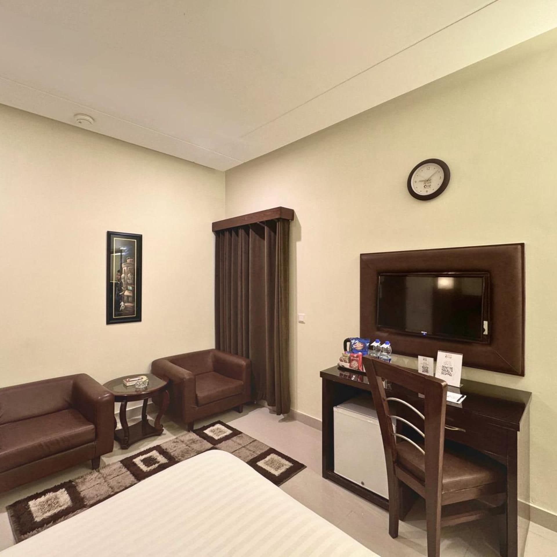 A hotel room with a bed, two sofas, a small table, a TV, and a clock on the wall.