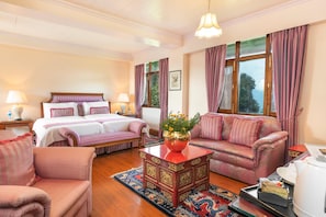 Une chambre d’hôtel avec un lit, un canapé, une petite table avec un vase et une fenêtre avec des rideaux.