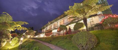 A hotel with a pathway leading to the entrance, surrounded by well-lit greenery and a night sky.