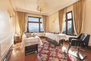 Une chambre d’hôtel avec deux lits, une moquette rouge à motifs, un fauteuil en cuir noir et une vue sur les montagnes par de grandes fenêtres.