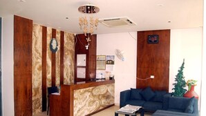 A reception area with a wooden reception desk, a blue sofa, and a decorative ceiling light. - Hotel Apaar (Diu)