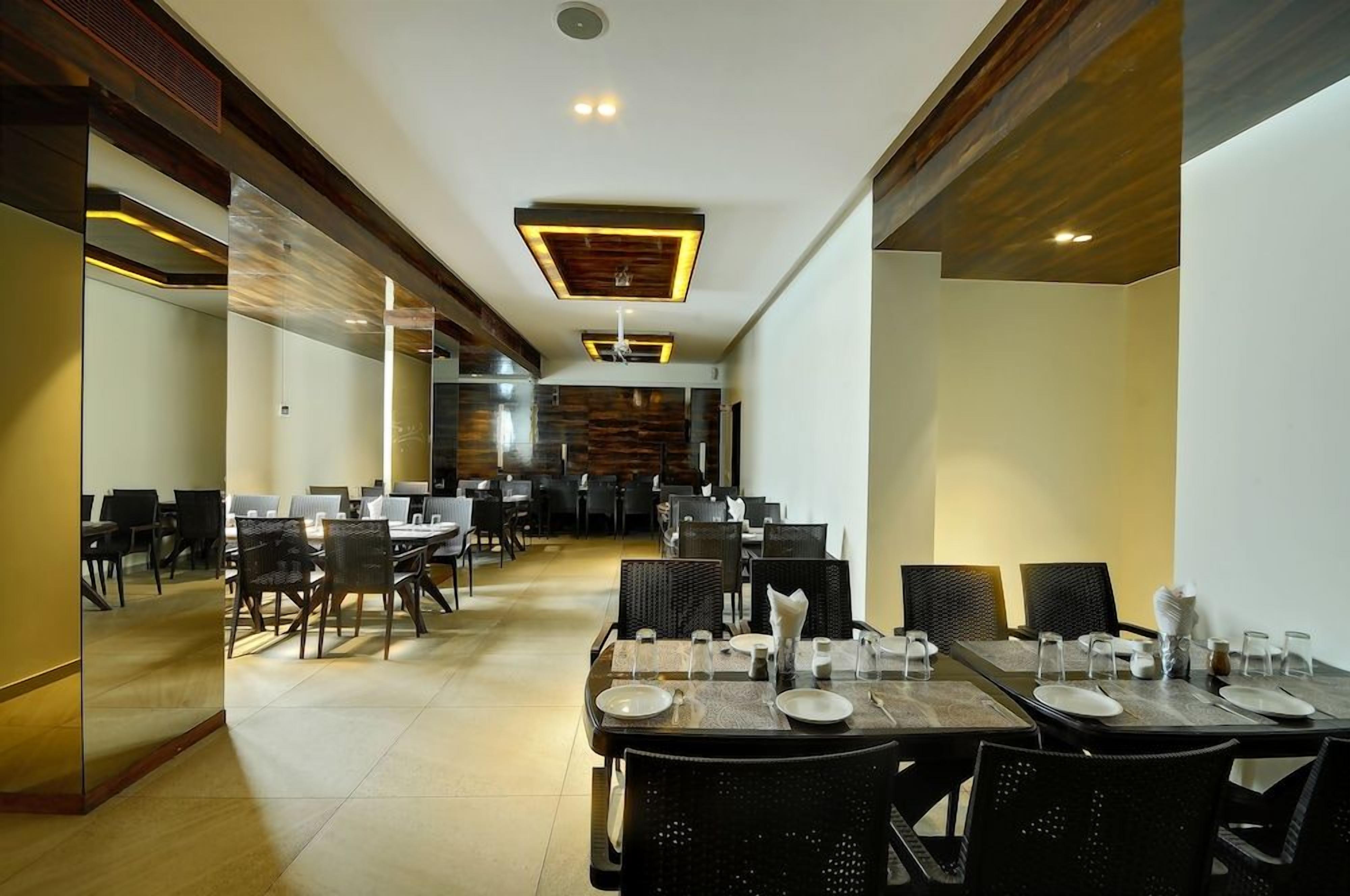 A spacious dining area with multiple tables and chairs, a modern ceiling design, and a visible kitchen area in the background.
