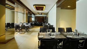 A spacious dining area with multiple tables and chairs, a modern ceiling design, and a central wall with a patterned design. - Hotel Apaar (Diu)
