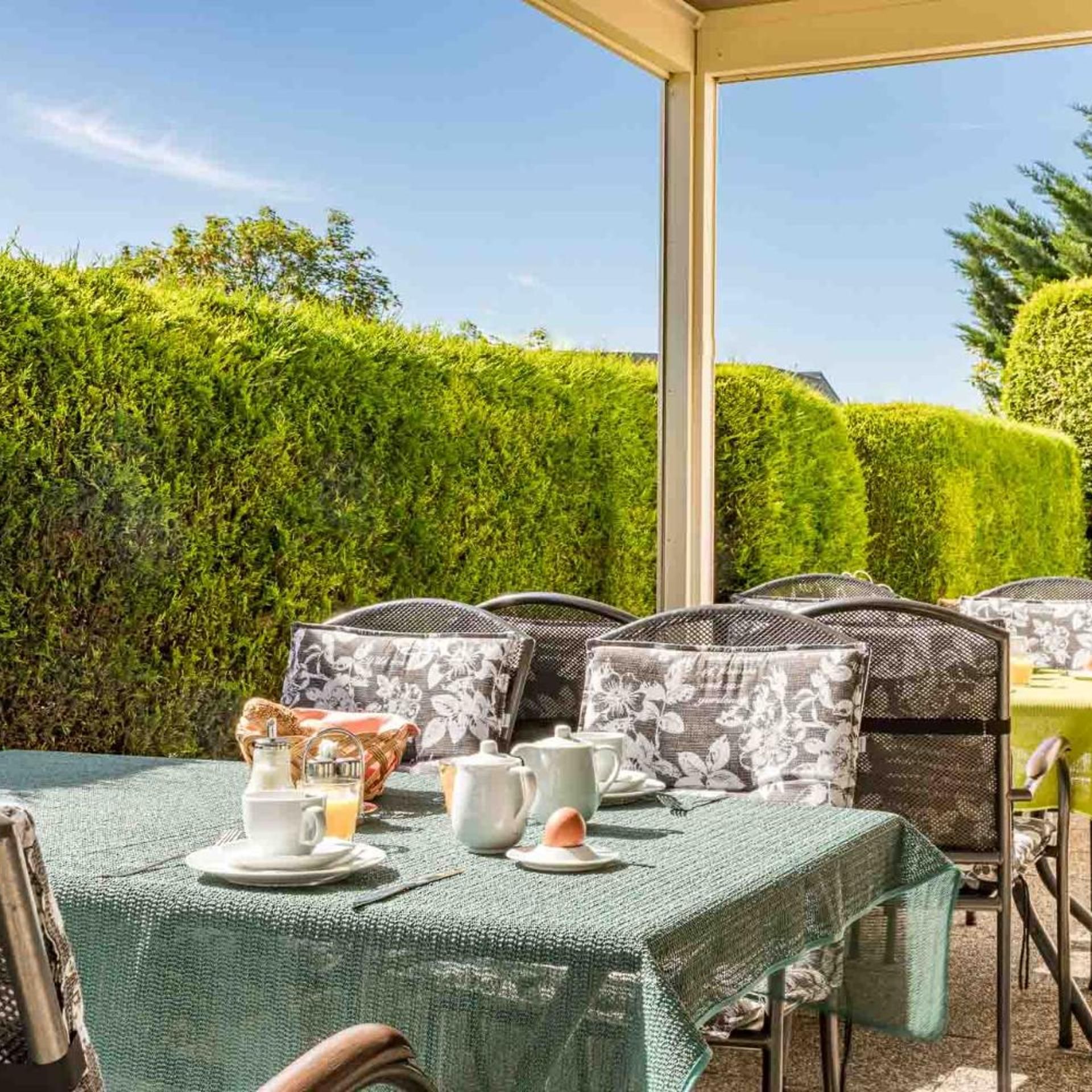 An outdoor dining area with tables set for breakfast, surrounded by neatly trimmed hedges.