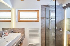 Un baño moderno con cabina de ducha de vidrio, un espejo grande y una ventana sobre el lavabo.
