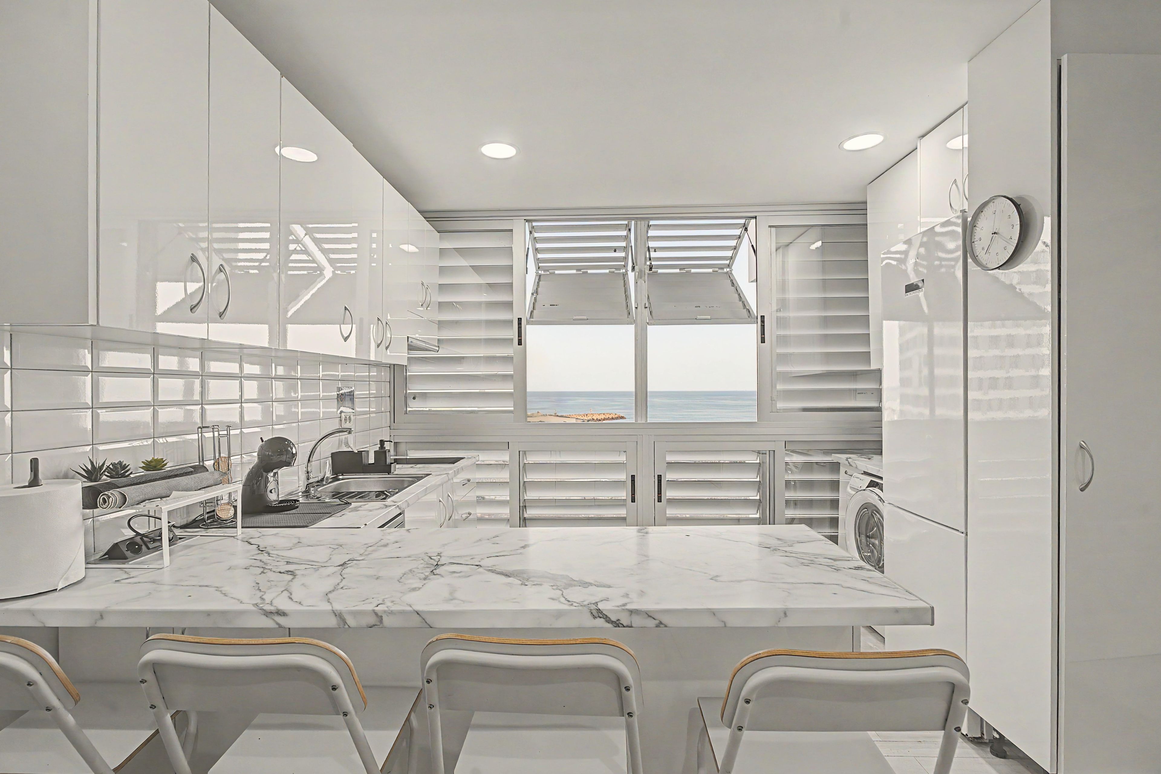 Een moderne keuken met een marmeren aanrechtblad, witte kastjes en uitzicht op het strand.