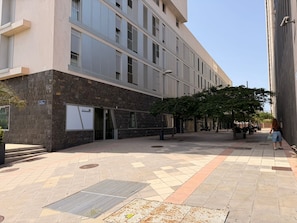 Un edificio con una facciata moderna, un ingresso coperto e un cortile pavimentato con alberi e zone relax.
