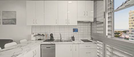 A modern kitchen with white cabinets, a dishwasher, and a view of the city through large windows.