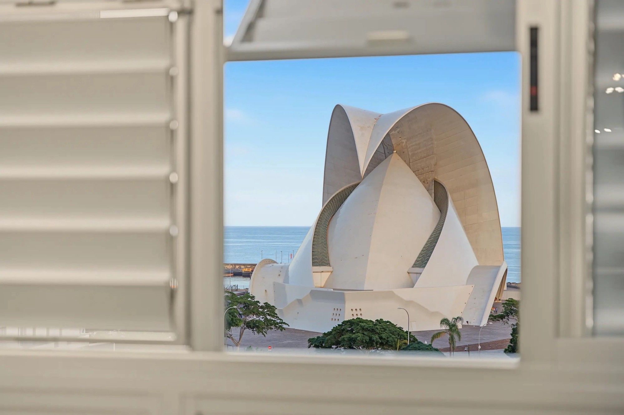 Een moderne architecturale constructie met een uniek, gebogen ontwerp, zichtbaar door een raam met horizontale zonwering.