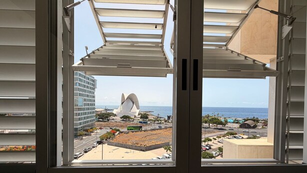 A window with a view of a coastal area, including a large white sculpture, buildings, and a clear sky. - Vacation Apartment 'Terraza del Atlántico' with Sea View and Wi-Fi (Santa Cruz de Tenerife)