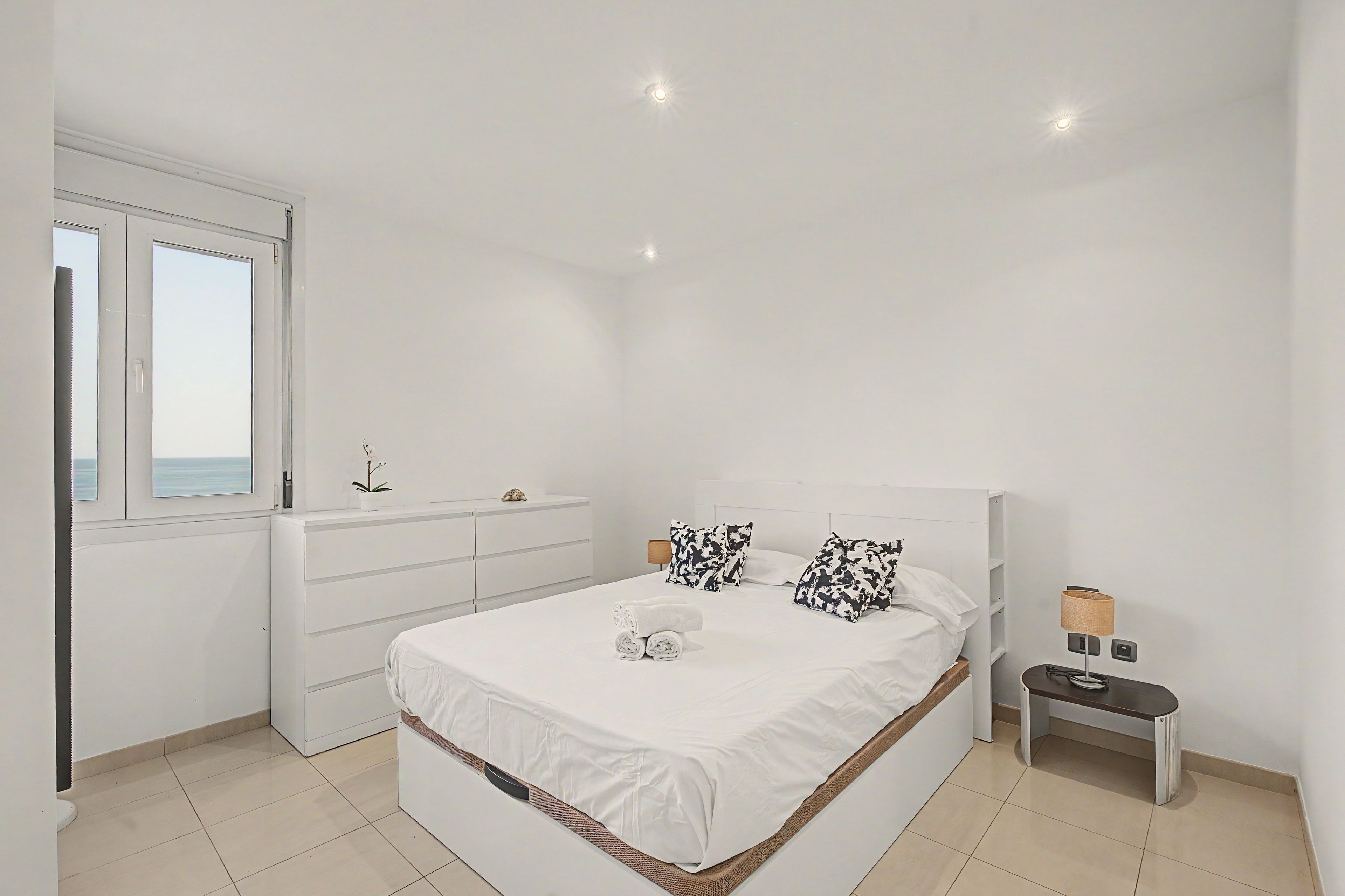 A bedroom with a bed, bedside tables, a dresser, a window with a view, and a lamp.