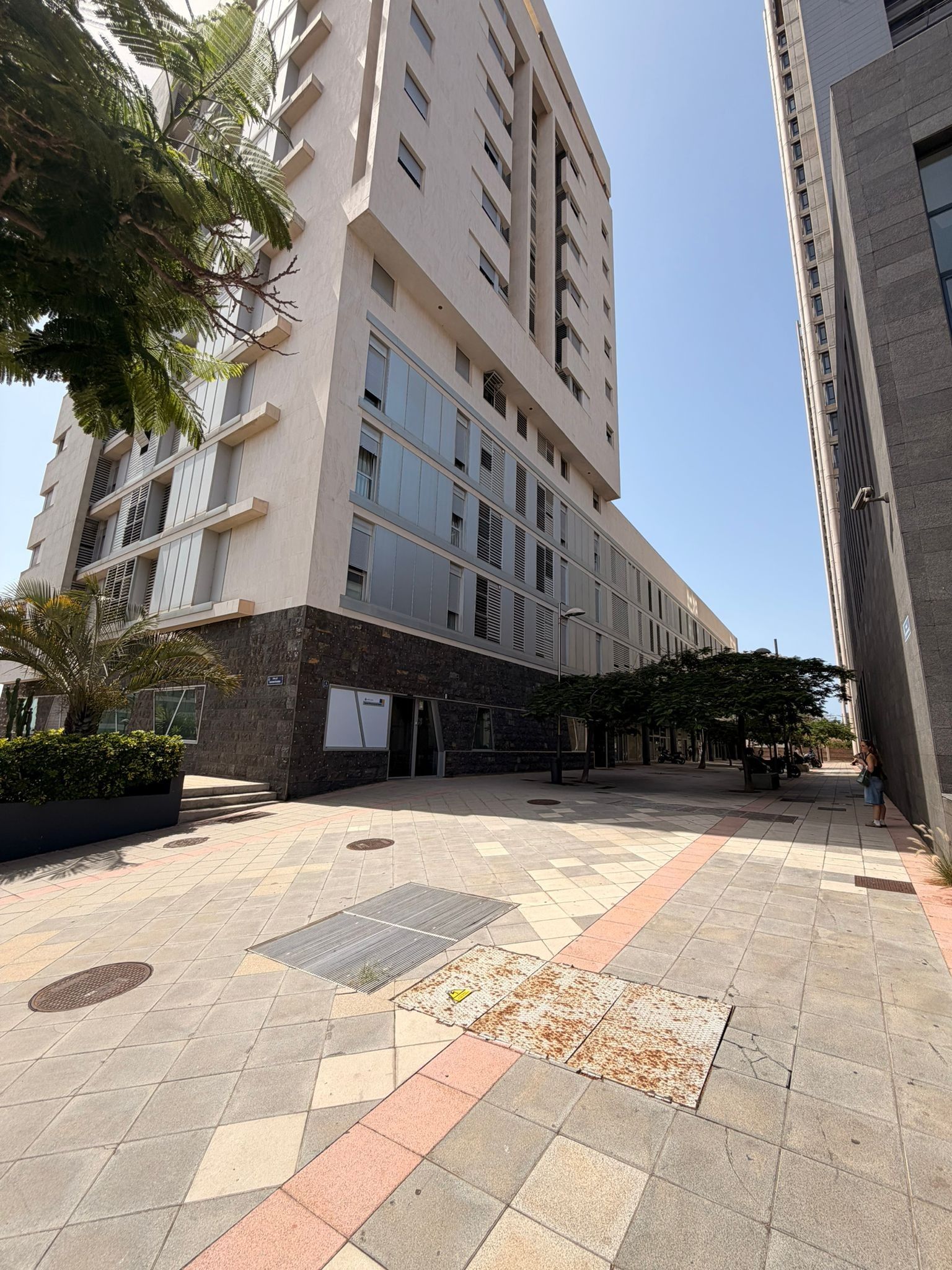Un edificio de varios pisos con fachada plana, ventanas amplias y un patio empedrado con piso estampado.