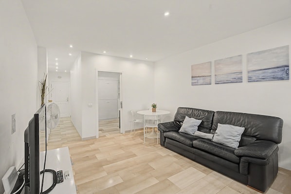 A modern living room with a black leather sofa, a flat-screen TV, and a dining area with a small table and chairs.