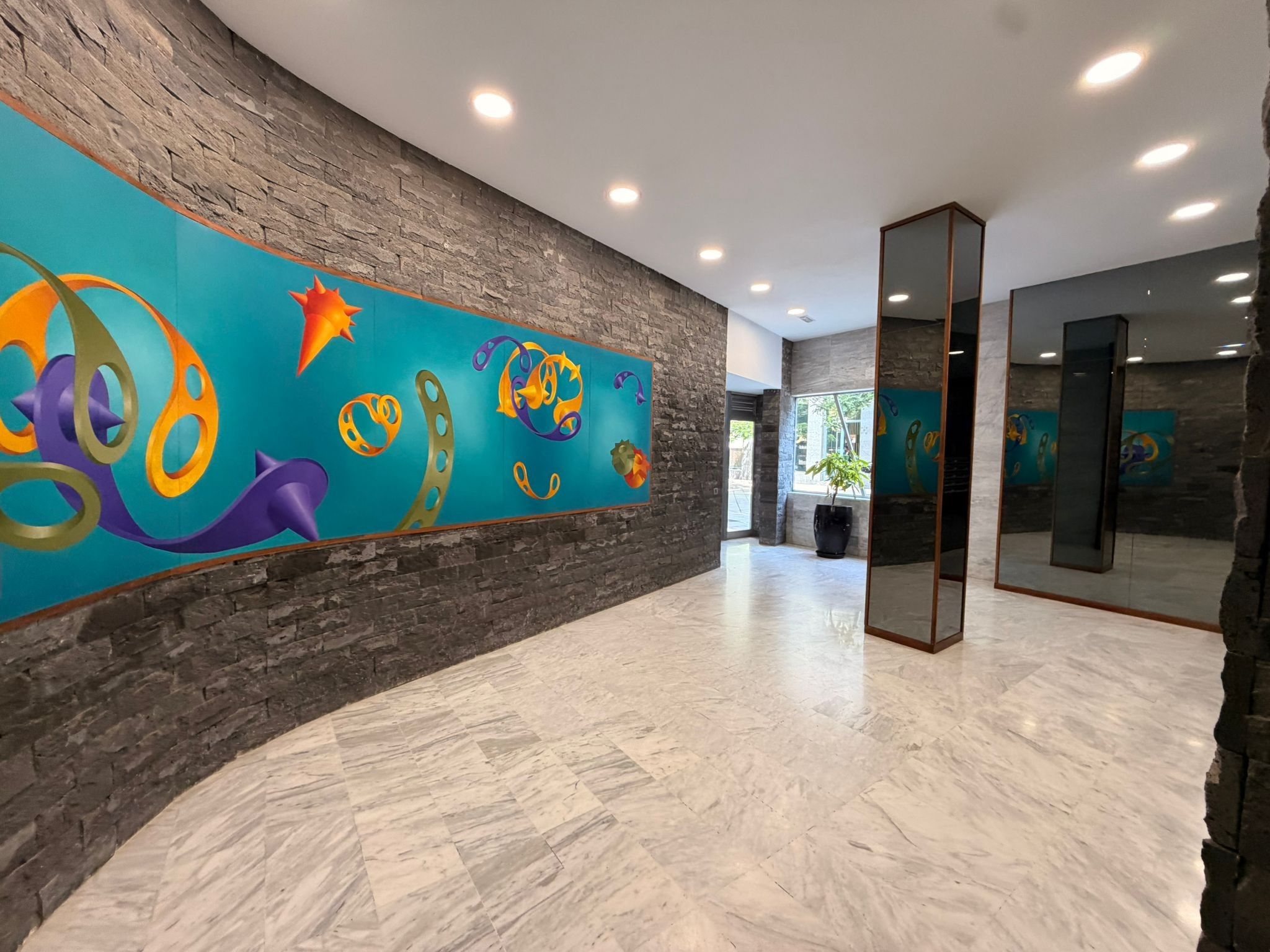 Un vestíbulo con un gran mural abstracto, paredes de piedra y piso de mármol.